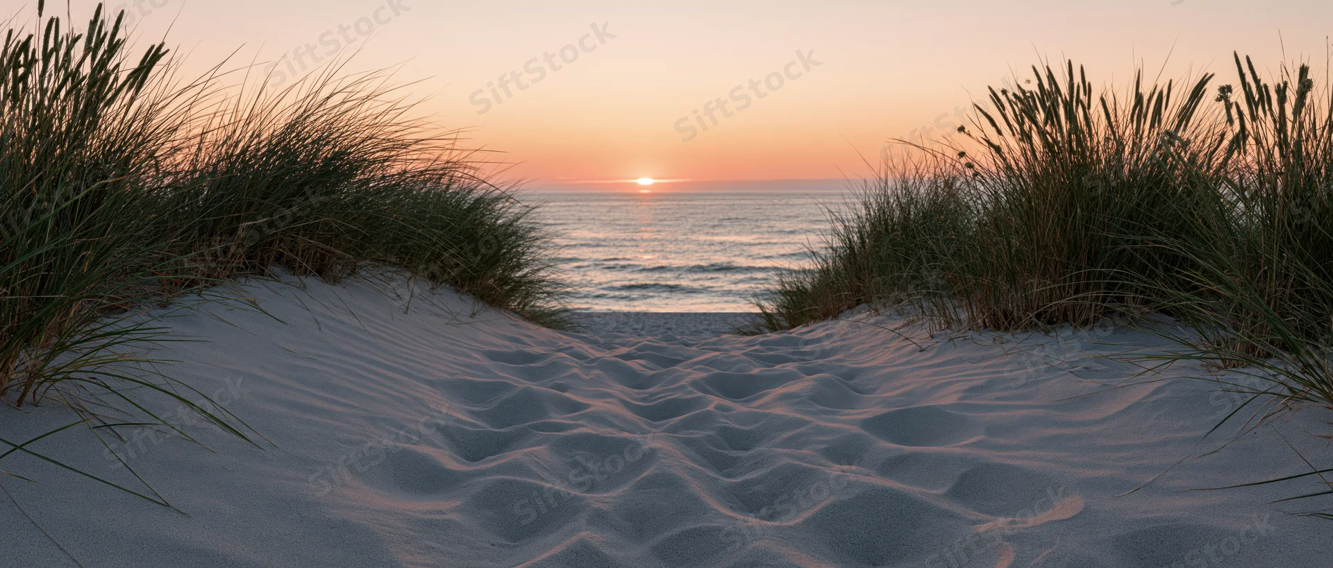 Sandy dunes with beachgrass framing a sunset over the ocean
