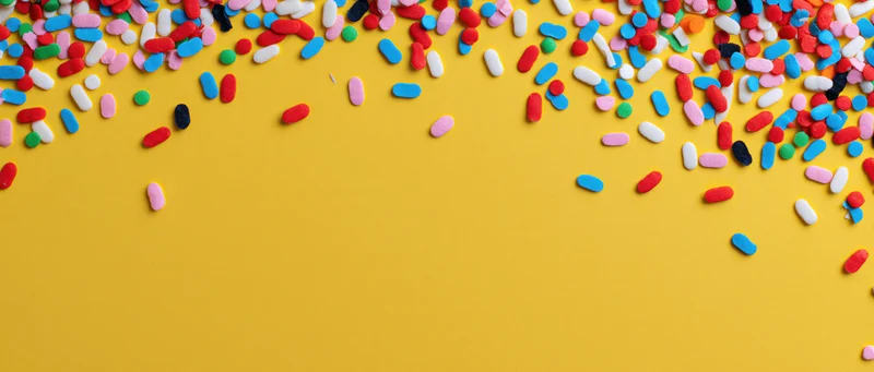 Colorful sprinkles scattered across yellow background with copyspace