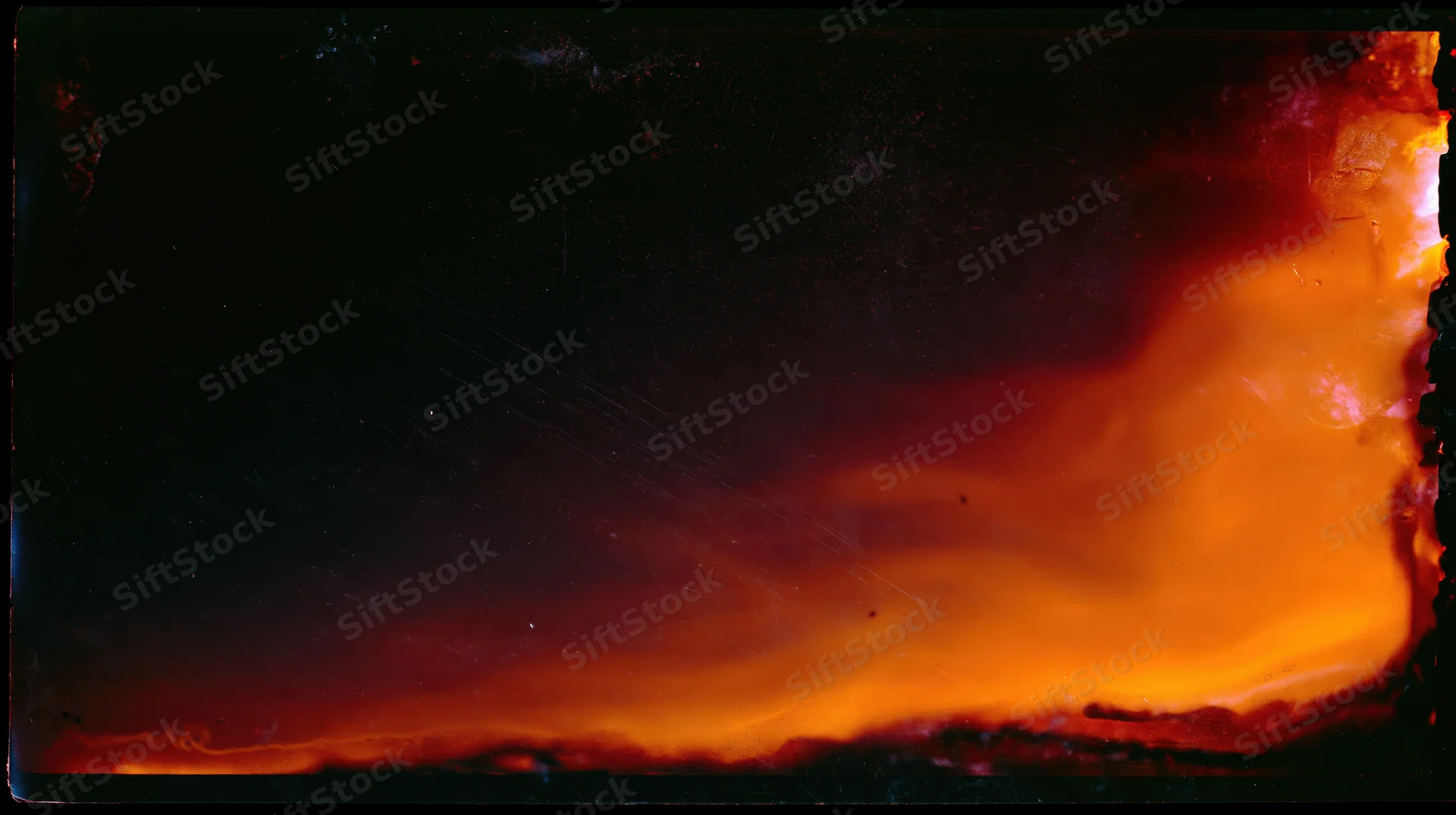 Intense fire burning across the frame at night with glowing orange flames and dark smoke against a black sky