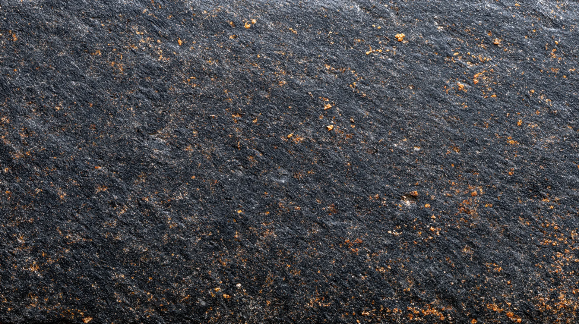 Closeup of dark slate rock surface with orange rust spots and natural texture