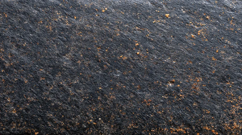 Closeup of dark slate rock surface with orange rust spots and natural texture