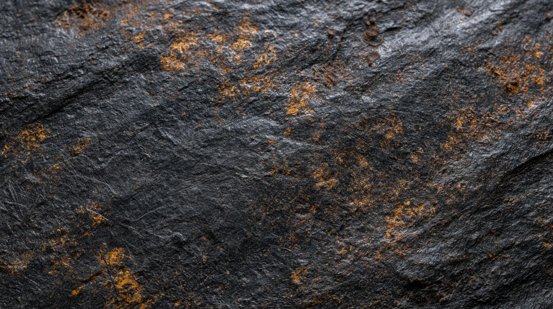 Dark textured rock surface with orange rust patches showing natural weathering and mineral oxidation