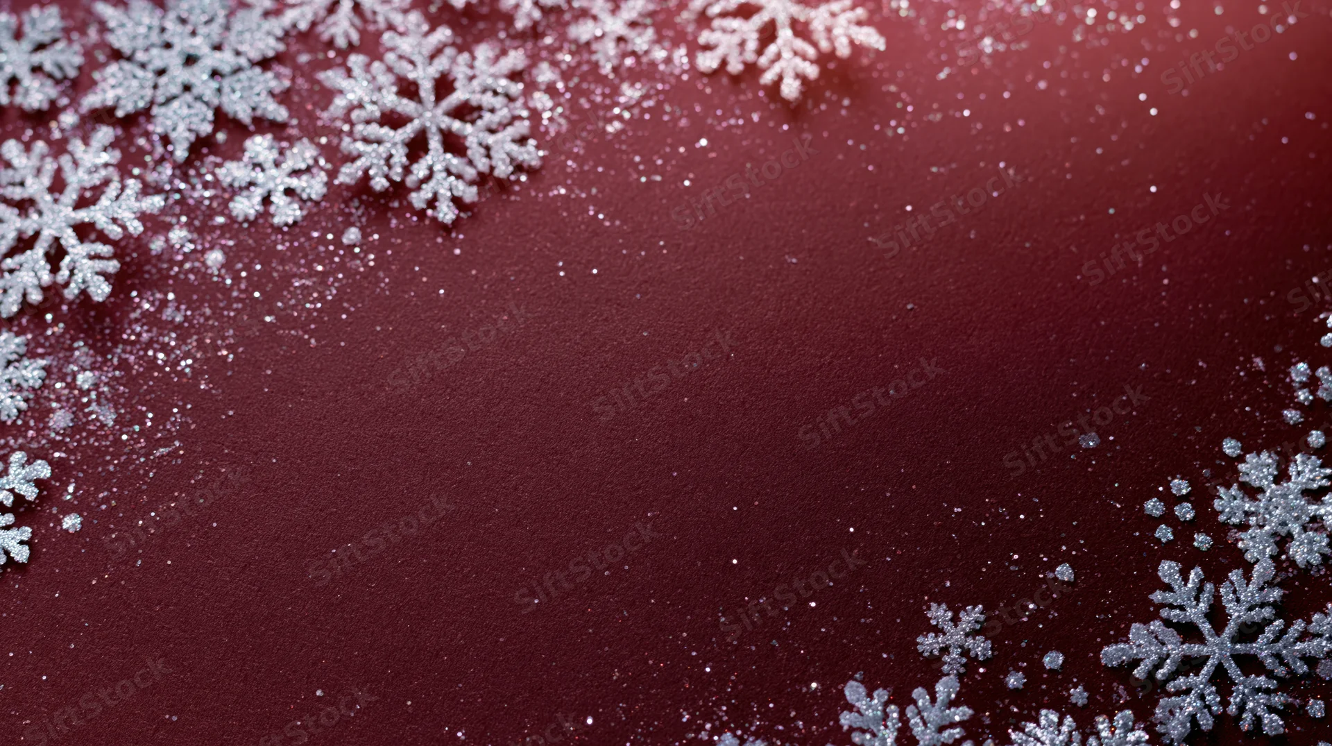 Silver snowflakes arranged in a corner border on a red glittery background with copyspace