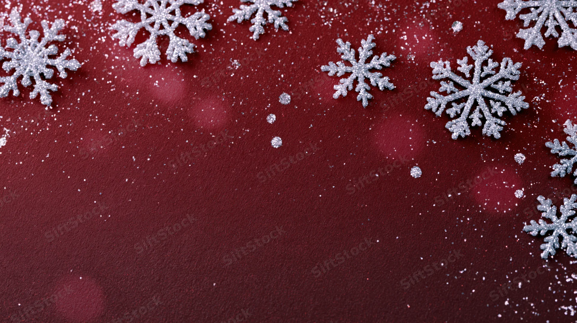 Silver glitter snowflakes arranged on red fabric background with bokeh lights and copyspace