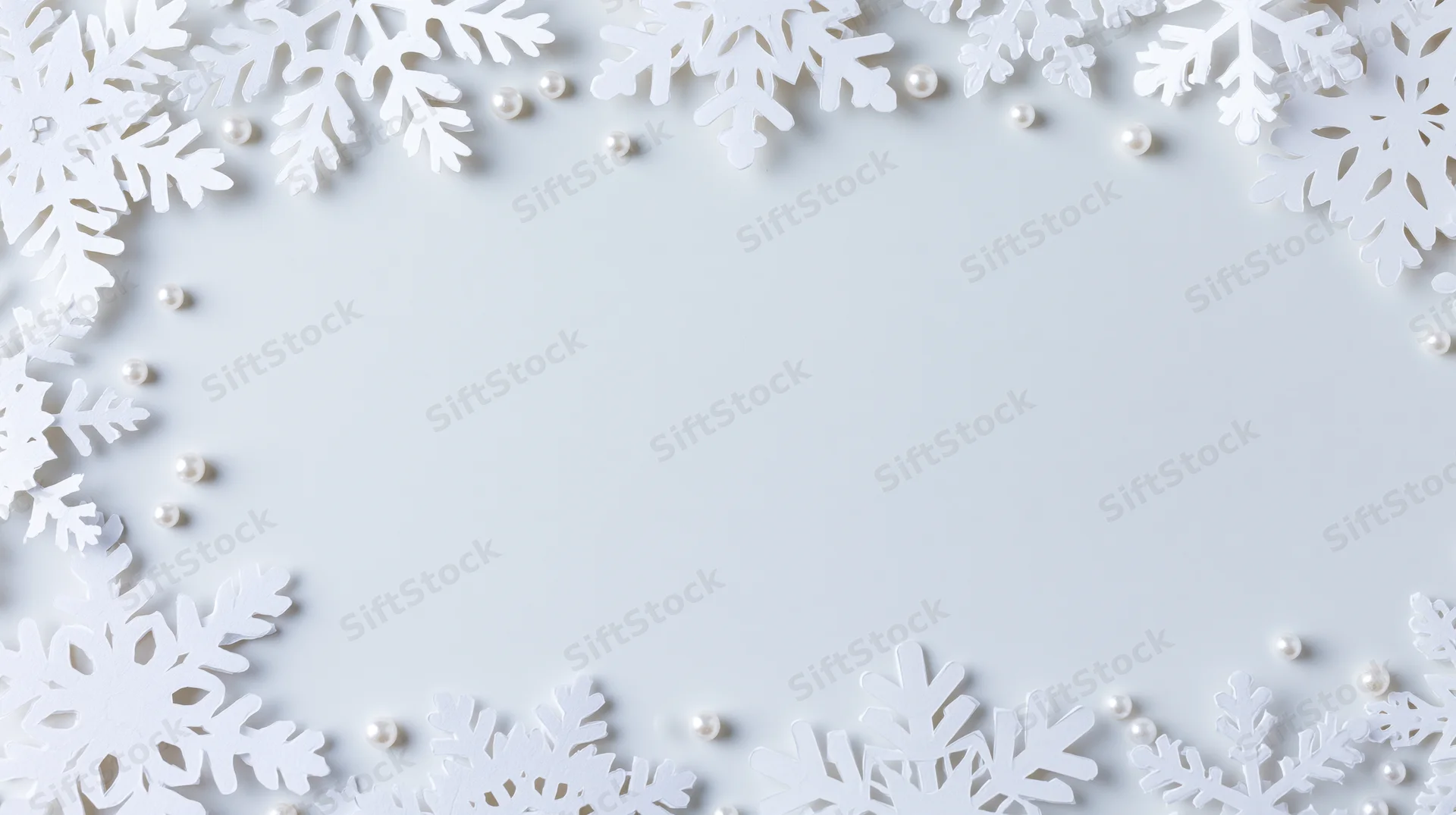 White paper snowflakes and pearls arranged in a border frame on a plain white surface with copyspace in the center