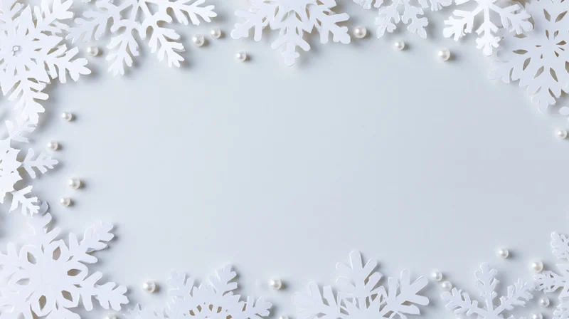 White paper snowflakes and pearls arranged in a border frame on a plain white surface with copyspace in the center