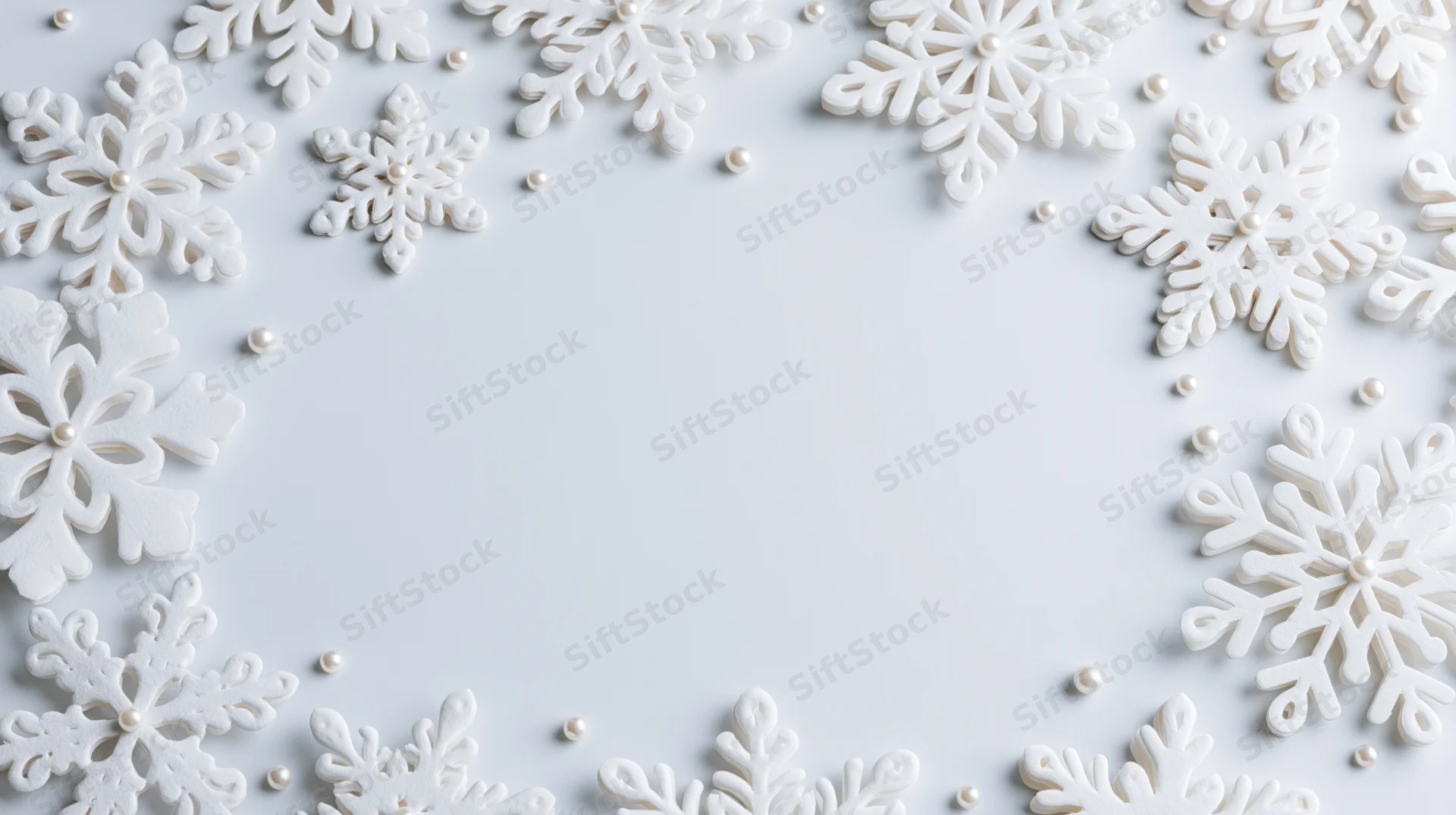 White snowflake decorations arranged in a border around a plain surface with scattered pearls, creating a festive holiday frame with copyspace in the center