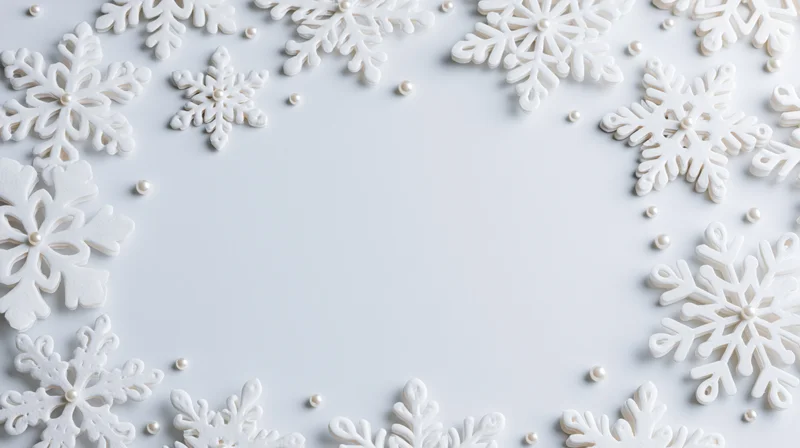 White snowflake decorations arranged in a border around a plain surface with scattered pearls, creating a festive holiday frame with copyspace in the center