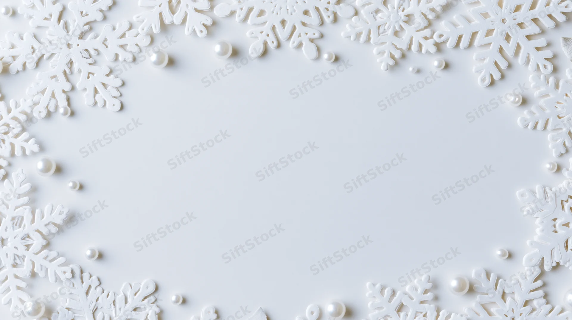 White snowflake decorations and pearls arranged in a border frame on a plain white surface with central copyspace