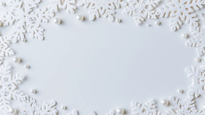 White snowflake decorations and pearls arranged in a border frame on a plain white surface with central copyspace
