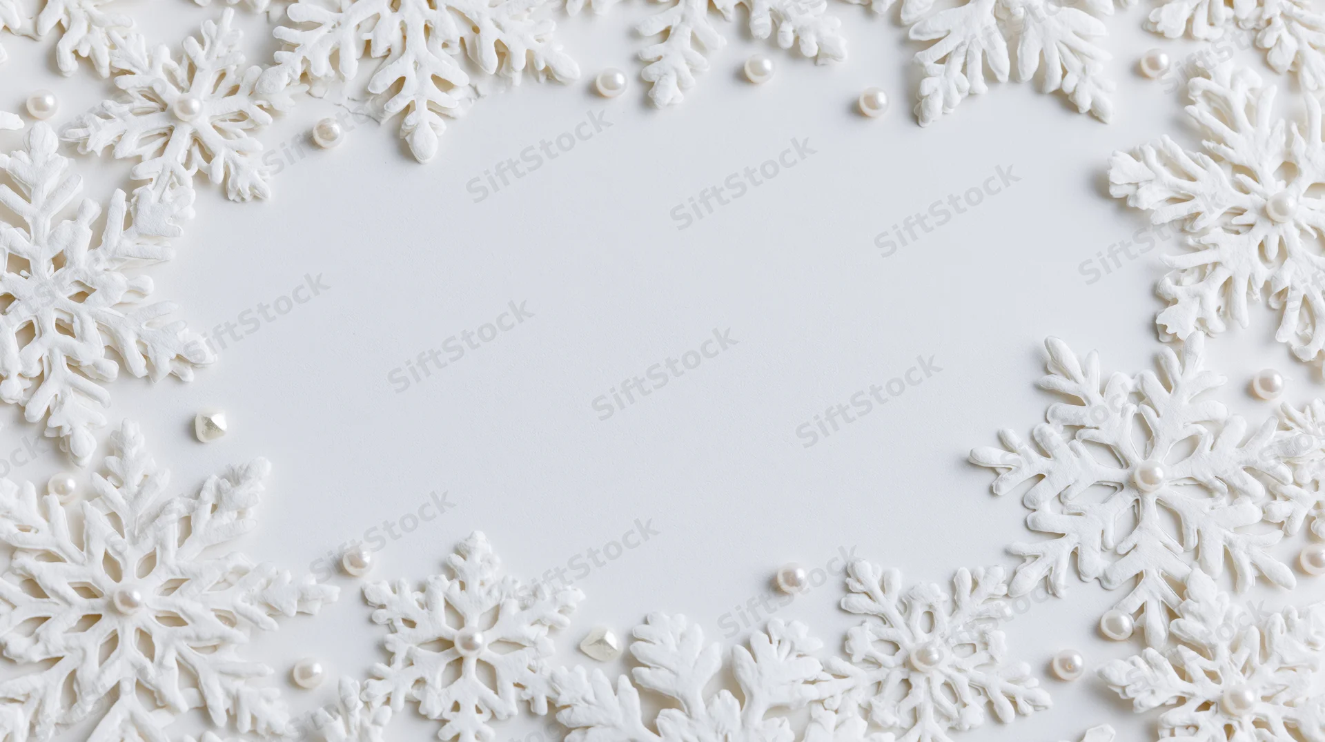 White snowflake decorations arranged in a border frame with pearls on a plain white surface