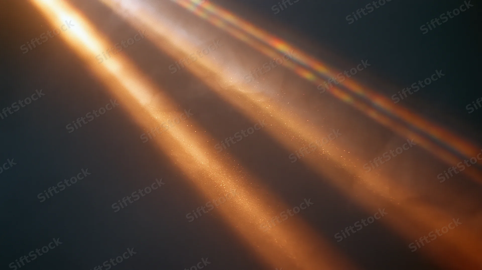 Diagonal beams of warm golden light with soft glow and floating particles against dark background