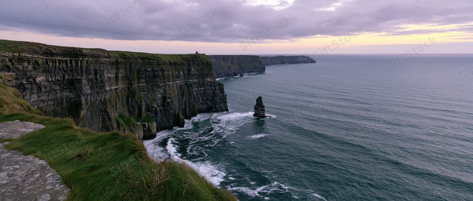 Rugged cliff face overlooking the ocean with waves crashing against sea stacks at dusk