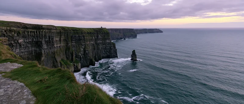 Rugged cliff face overlooking the ocean with waves crashing against sea stacks at dusk