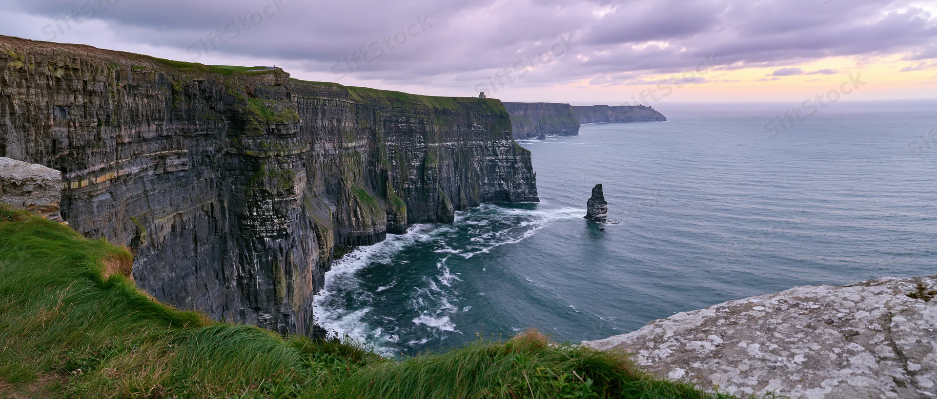 Rugged cliff face overlooking ocean with waves crashing below at dusk
