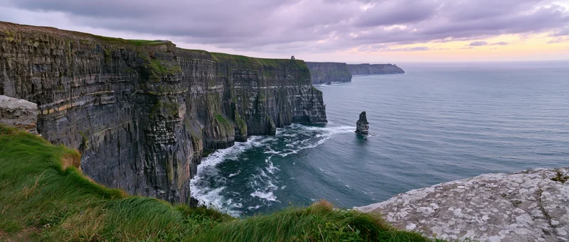 Rugged cliff face overlooking ocean with waves crashing below at dusk