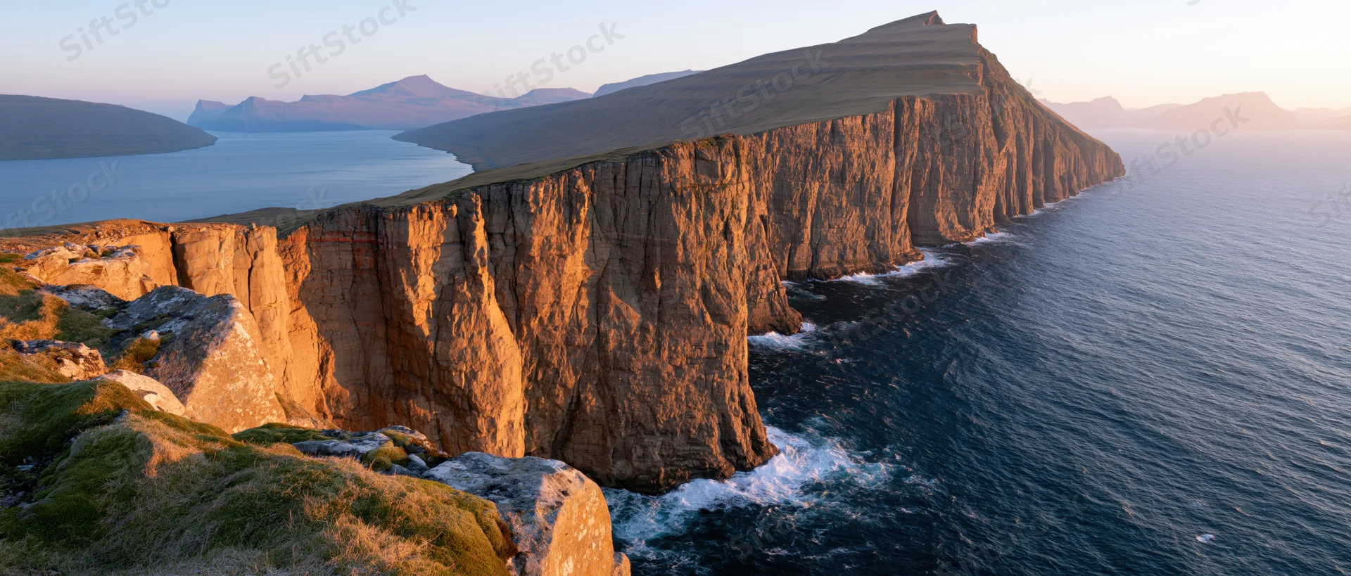 Rugged cliff face along the coastline at sunset with ocean waves crashing below