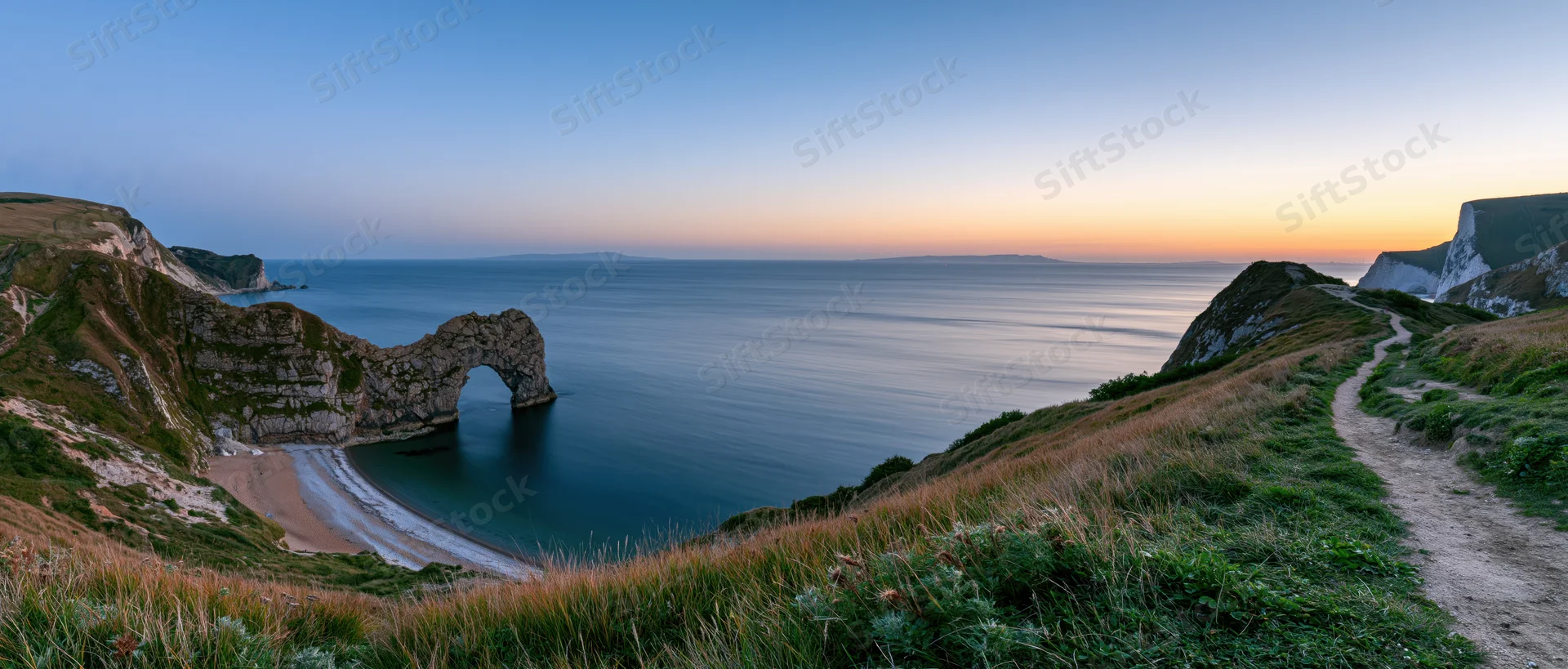 Natural rock arch over calm sea at sunset along coastal cliff path