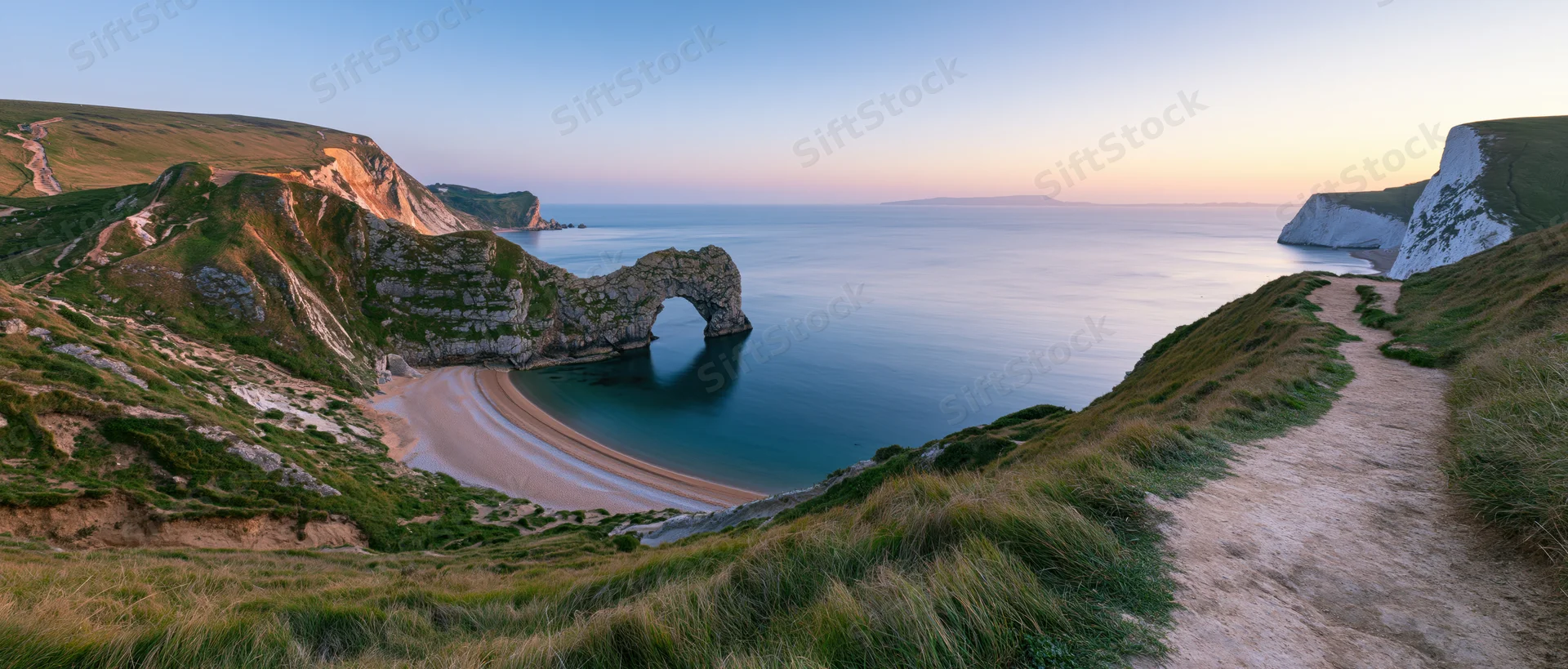 Natural rock arch over a sandy cove at sunset along a coastal cliff path