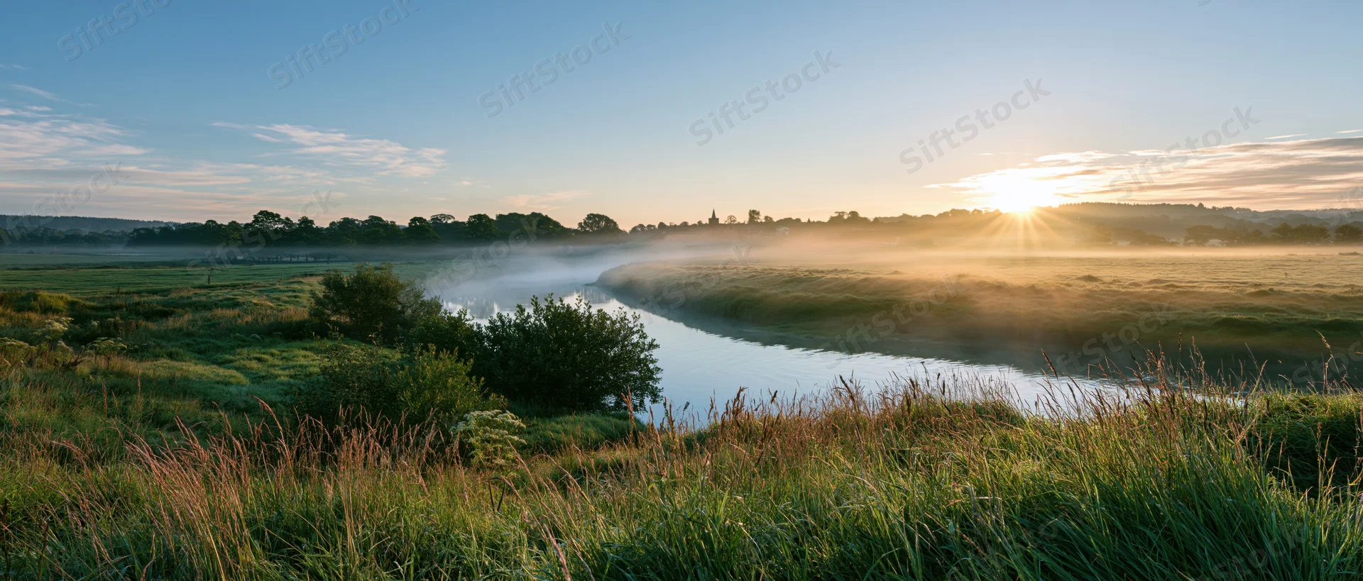 Misty river winding through green meadow at sunrise