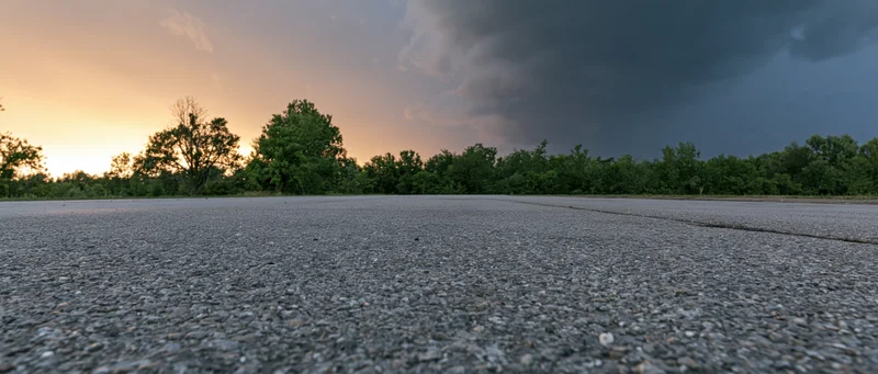 Asphalt road stretching toward a stormy horizon at sunset with trees lining the edge