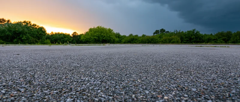 Gravel road surface stretching toward a tree-lined horizon under a stormy sunset sky