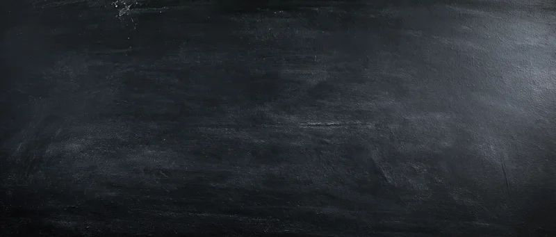 Dark textured blackboard surface with chalk residue and smudges, showing signs of use and wear