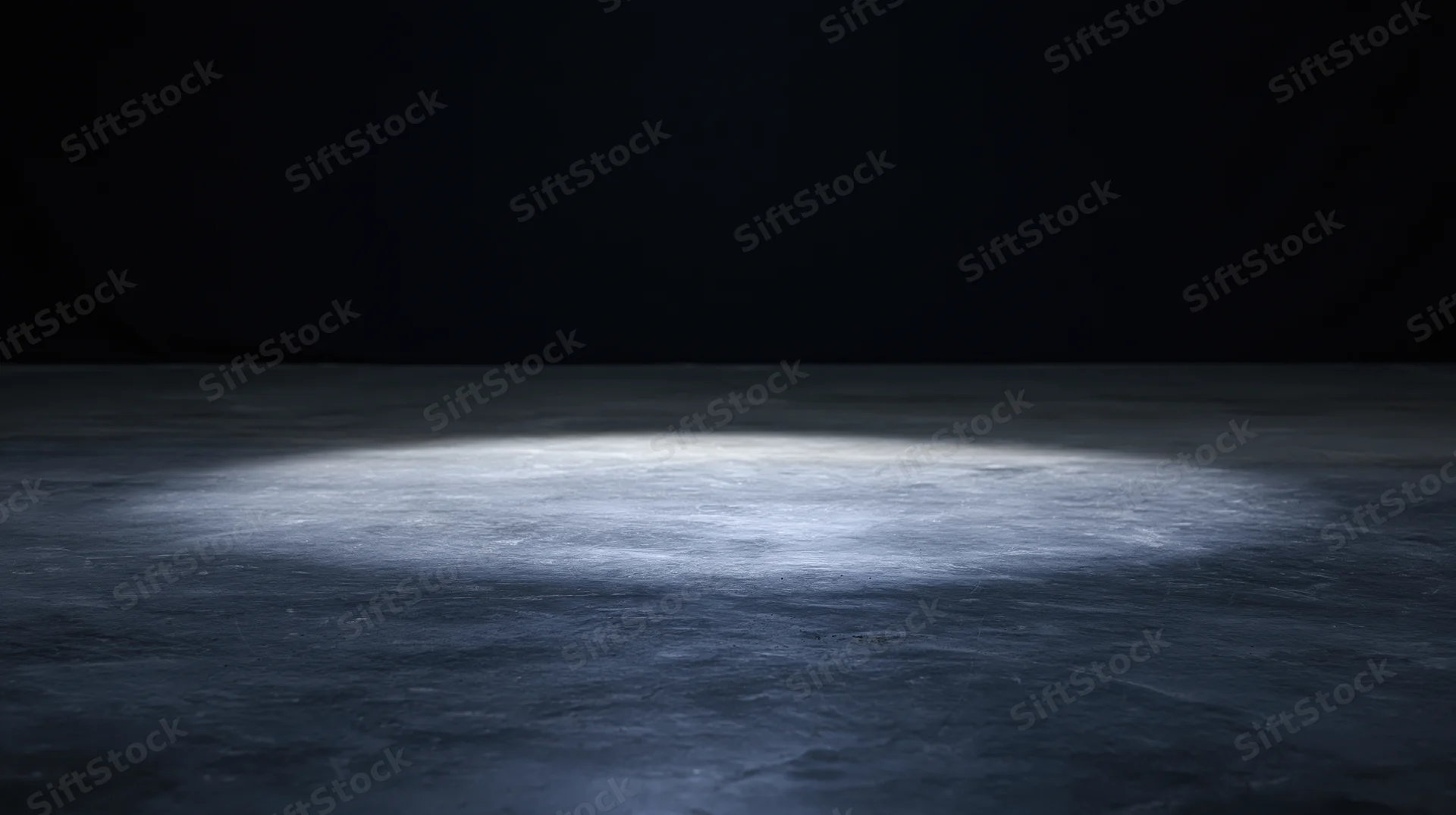 Spotlight on empty concrete floor in dark studio space
