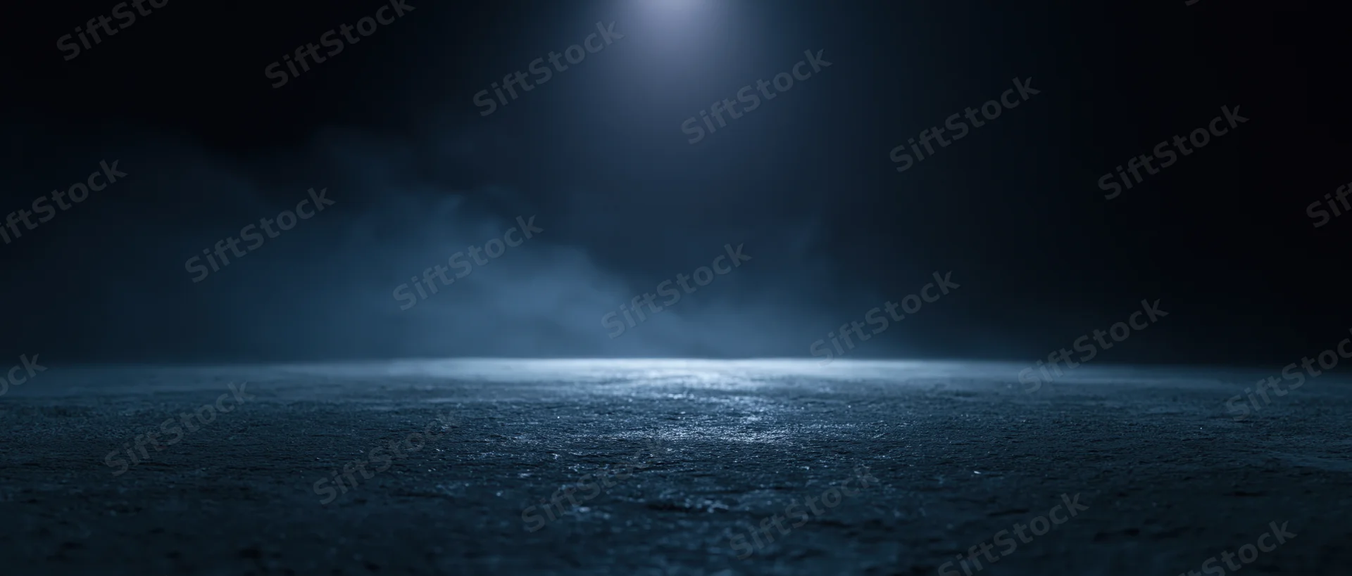 Spotlight illuminating wet asphalt at night with fog drifting across the surface