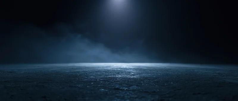 Spotlight illuminating wet asphalt at night with fog drifting across the surface