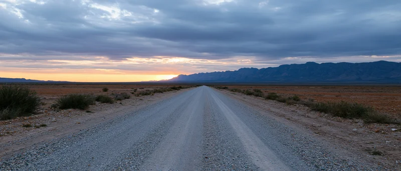 Gravel road stretching into the desert at sunset with mountains on the horizon