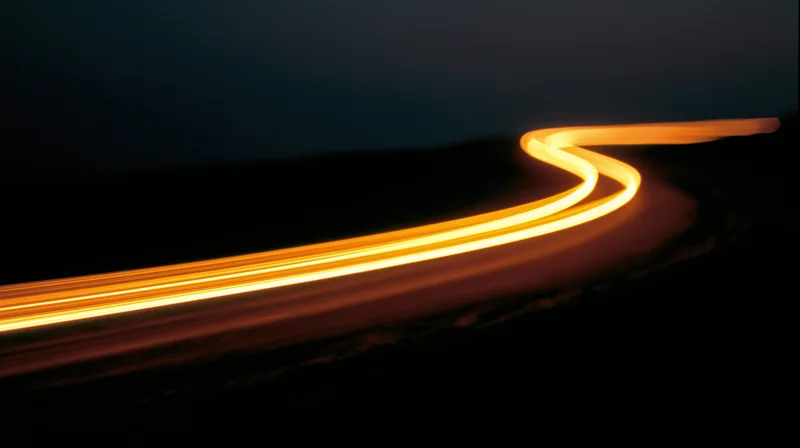 Glowing light trails from vehicles moving along a winding road at night