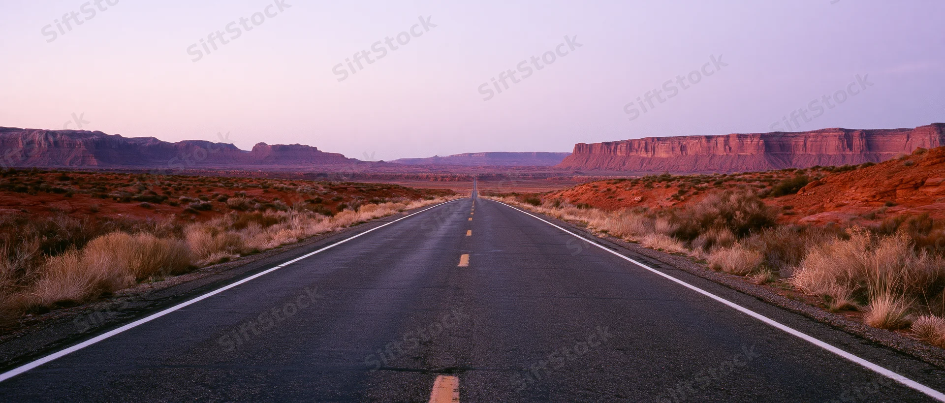 Straight asphalt road stretching into the desert landscape at twilight with red rock formations on either side