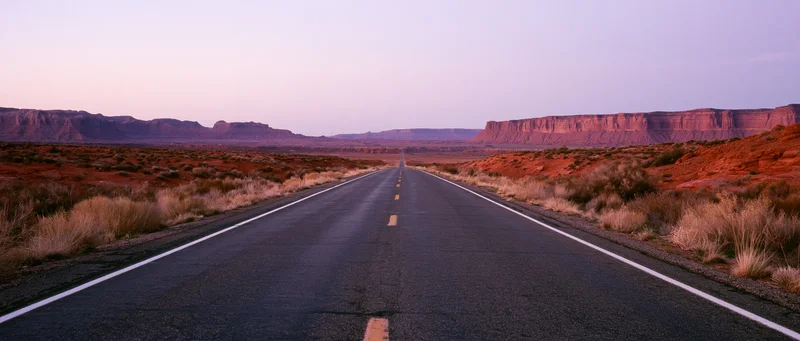 Straight asphalt road stretching into the desert landscape at twilight with red rock formations on either side