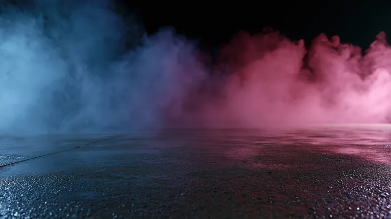 Colored smoke drifting over a wet concrete floor in a dark studio space