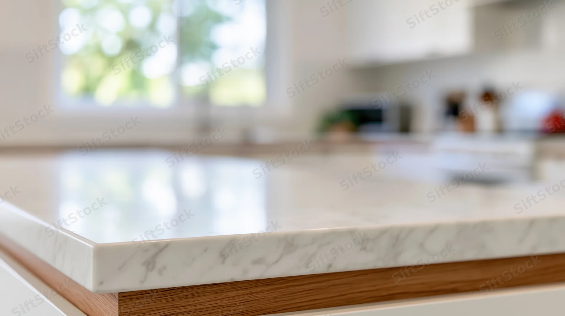 Close-up of a white marble kitchen countertop with wood edge and blurred background showing window and appliances