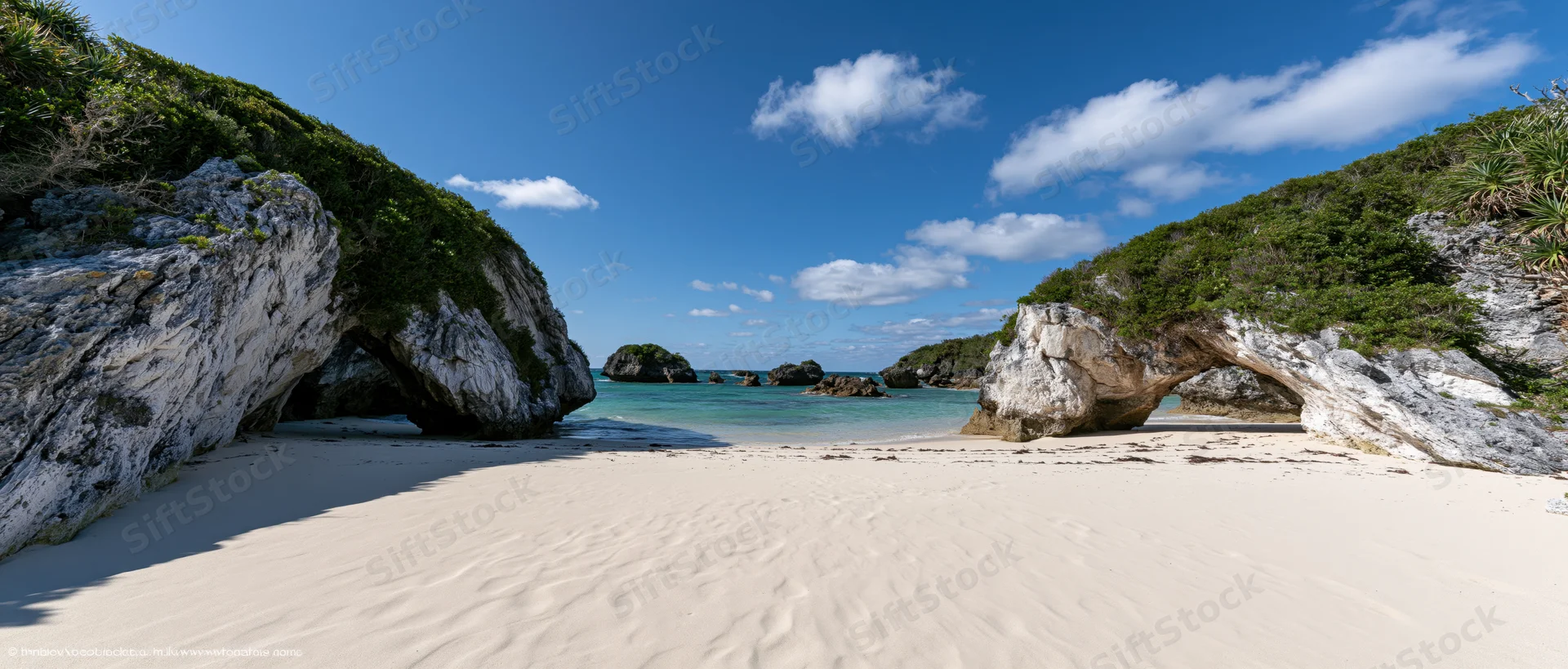 White sandy beach framed by natural rock arches under a blue sky with scattered clouds near turquoise ocean waters