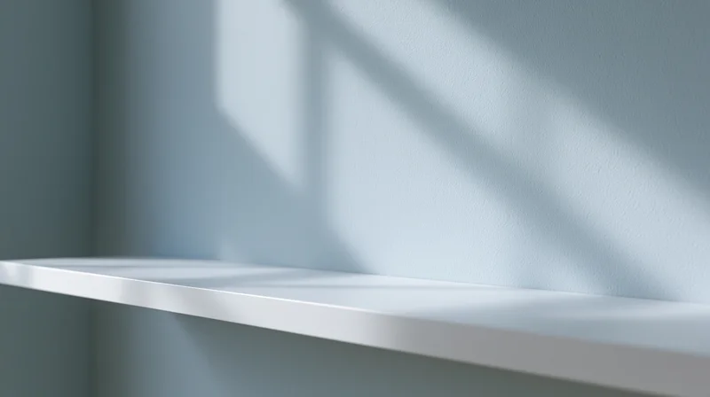 Empty white shelf mounted on a blue wall with sunlight casting shadows in a minimalist interior