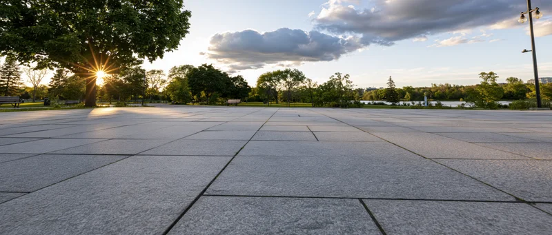 Paved plaza in a park at sunset with trees and river in the background