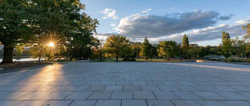 Sunlit stone plaza surrounded by trees and park greenery at sunset