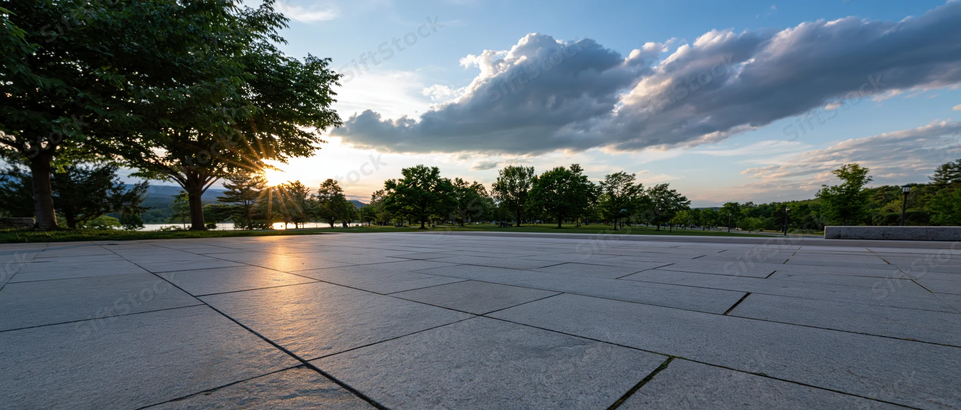 Stone plaza at sunset with trees and sky reflecting on the pavement