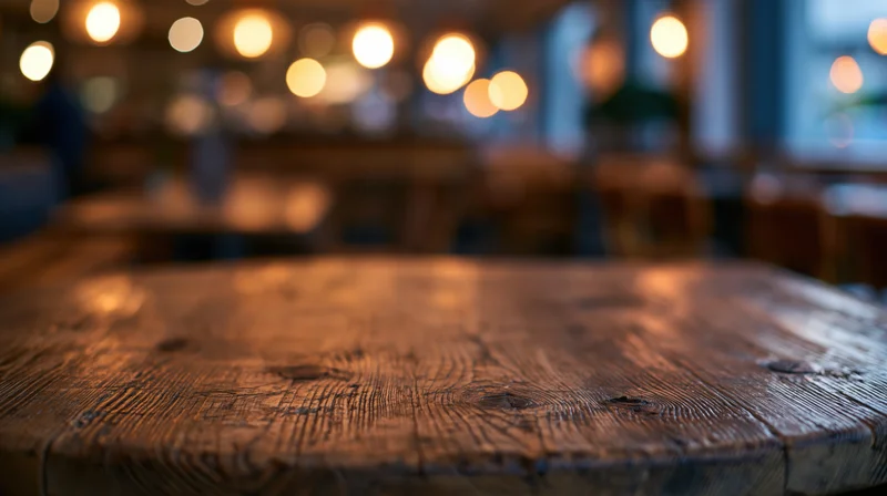 Wooden table surface in a warmly lit restaurant interior with blurred background lights