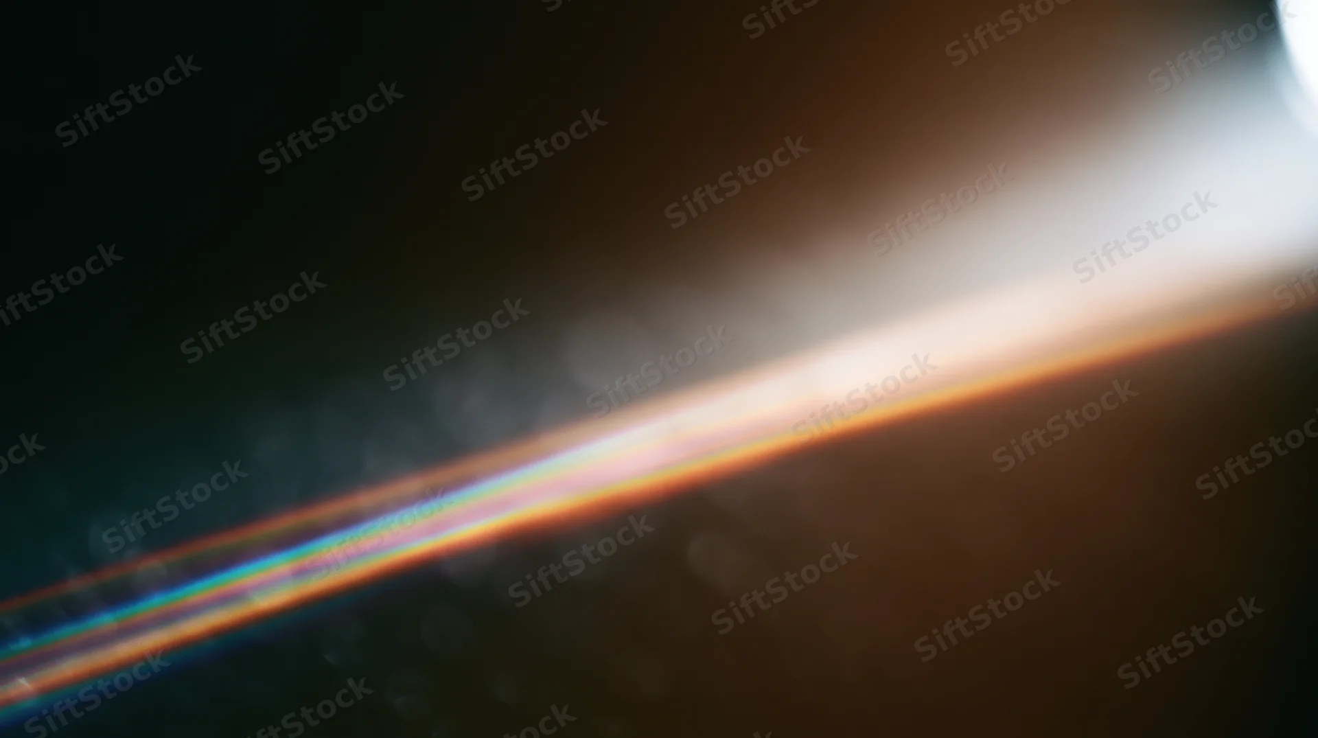Bright light flare with rainbow spectrum across dark background, creating soft bokeh and lens flare effect