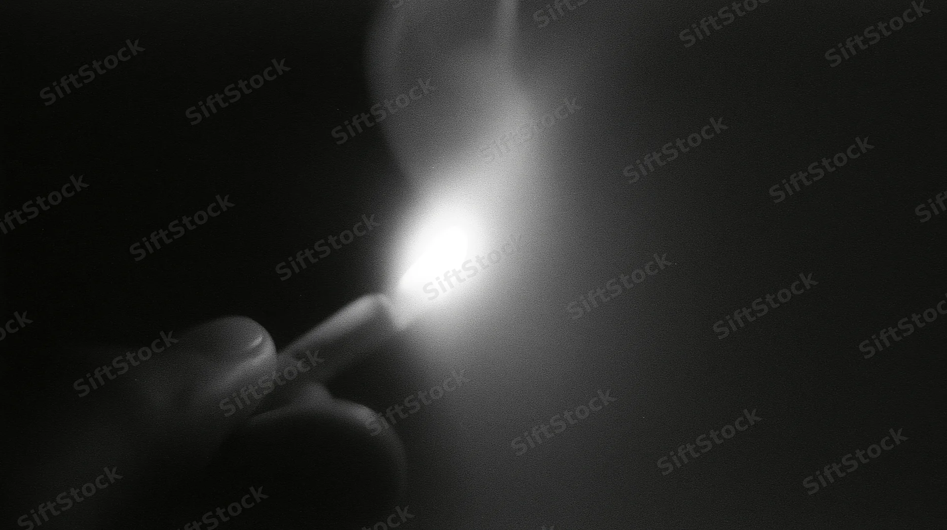 Hand holding lit match in dark, flame glowing brightly with smoke rising