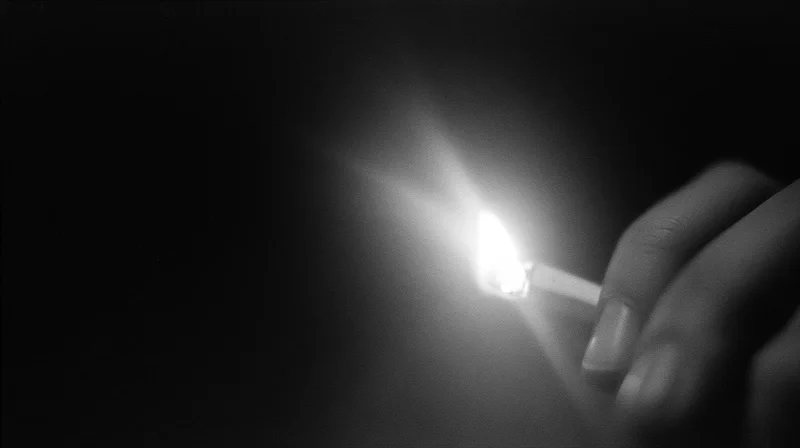 Hand holding lit match in dark space