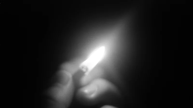 Hand holding lit lighter in darkness
