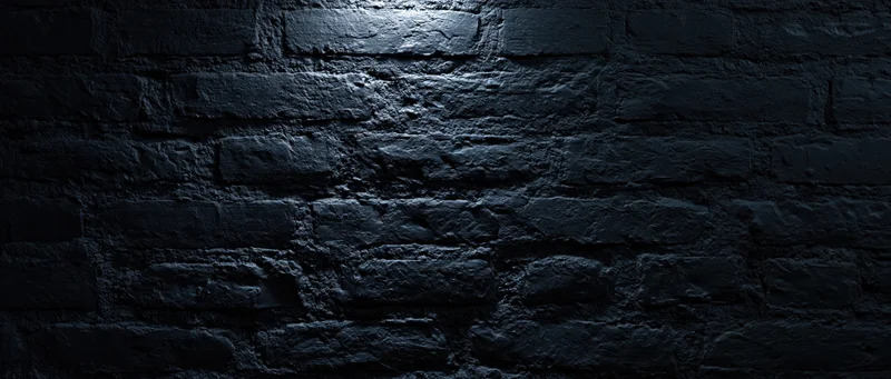 Dark textured brick wall illuminated by spotlight in dim interior space