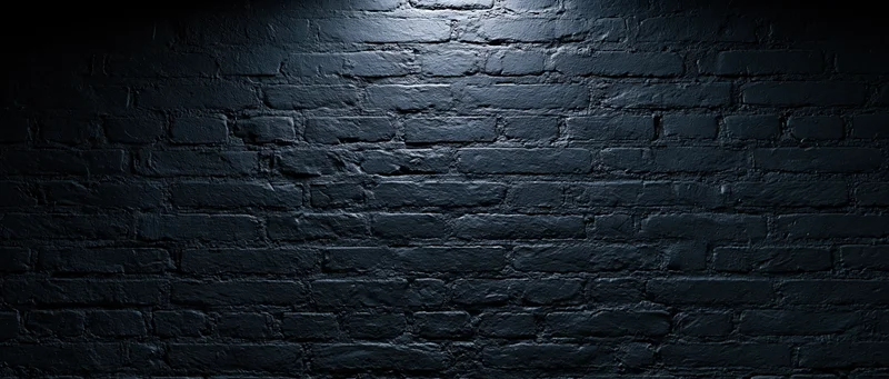 Dark brick wall illuminated by spotlight with shadows and copyspace