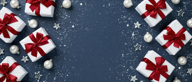 White gift boxes with red ribbons arranged around a dark blue snowy background with silver stars and ornaments