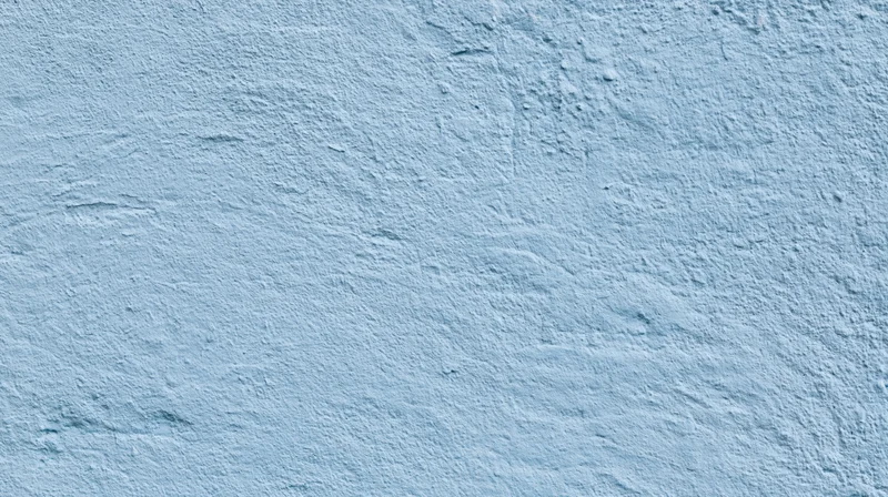 Close-up of a light blue plastered wall surface with rough texture and subtle imperfections
